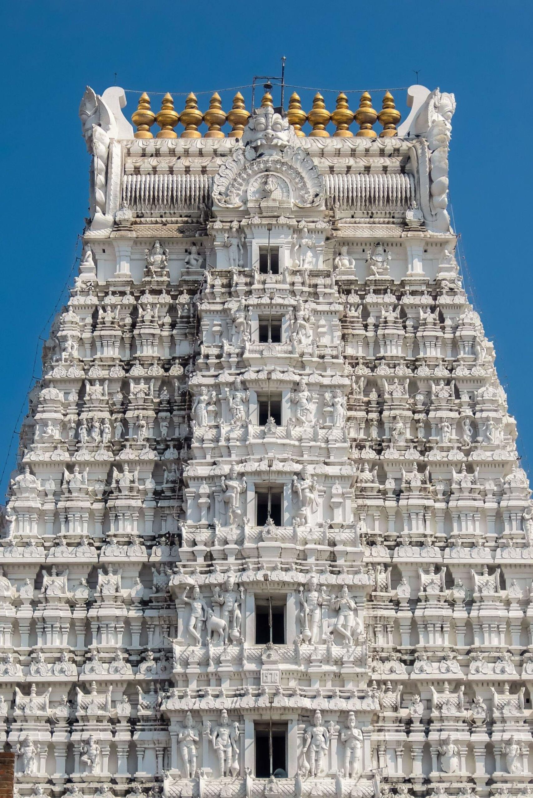 White stone temple gopuram with intricate carvings against a clear blue sky