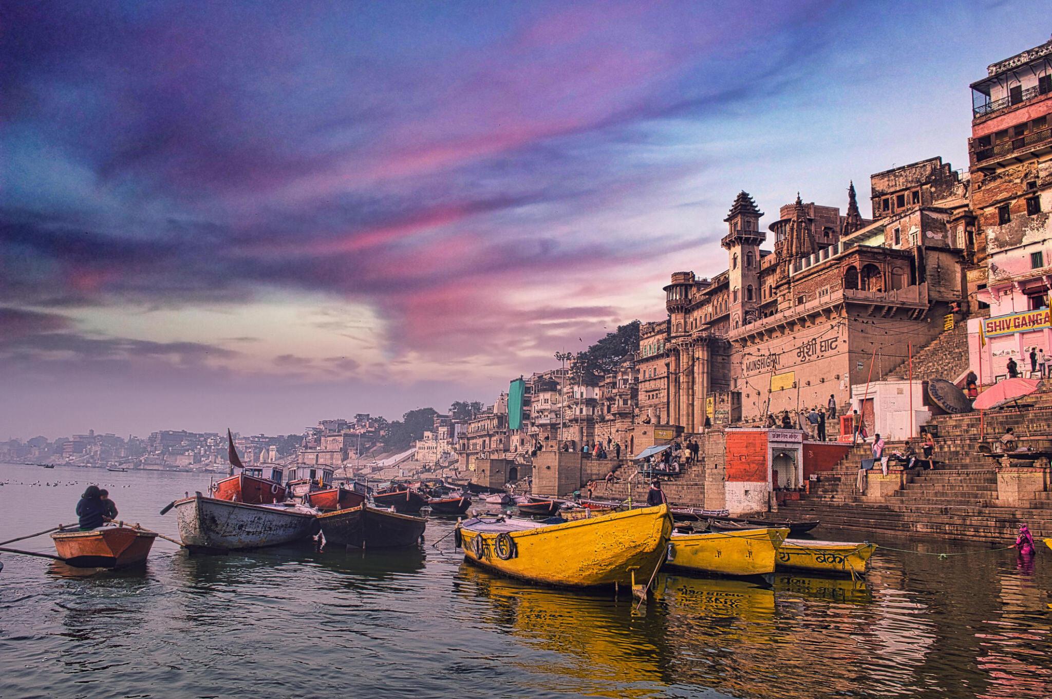 Colorful boats anchored along the ghats of Prayagraj on the Ganges River at sunset with historic buildings in the background