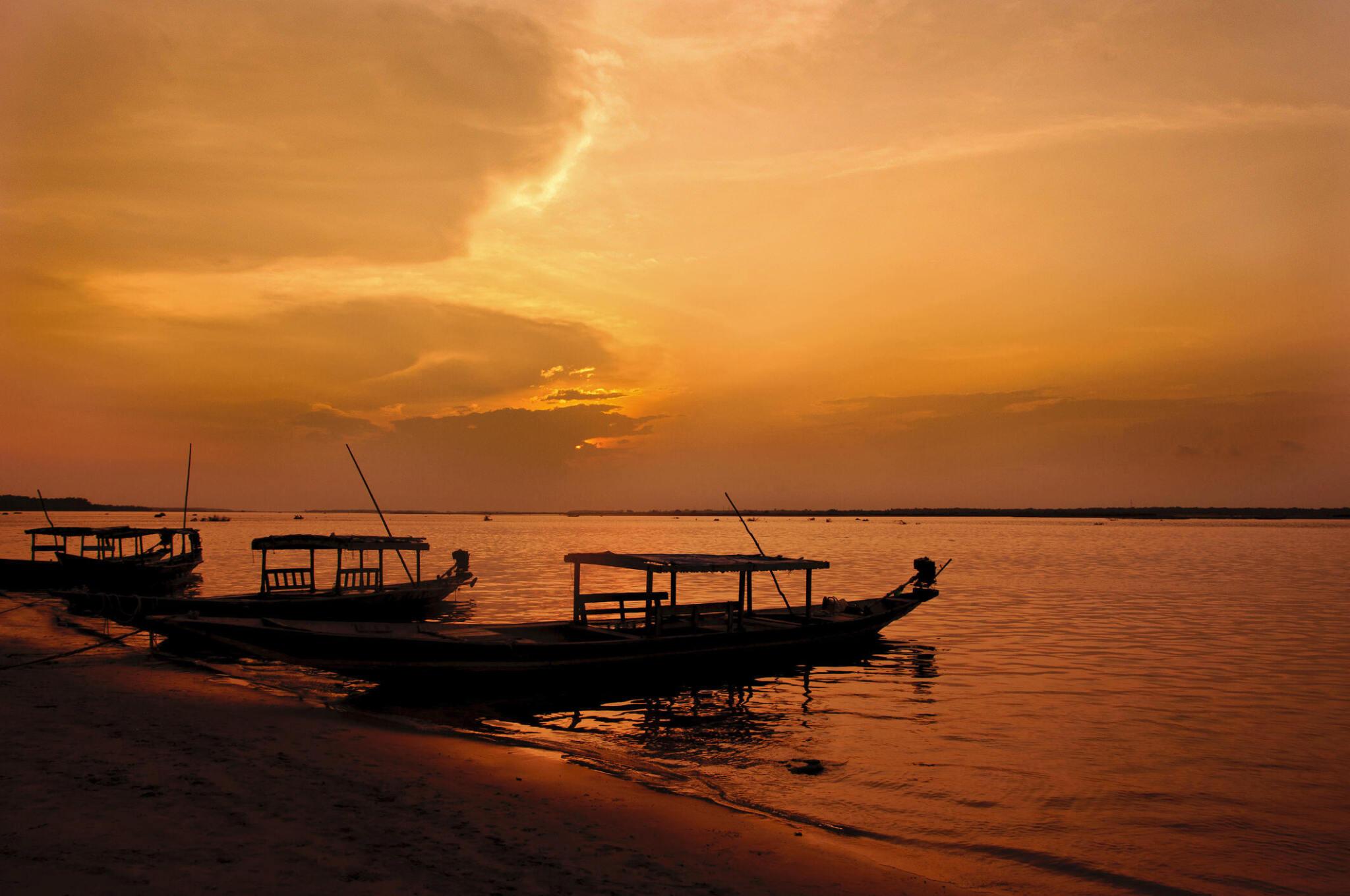 Traditional boats anchored by the shore under a golden sunset near Barbil, Odisha