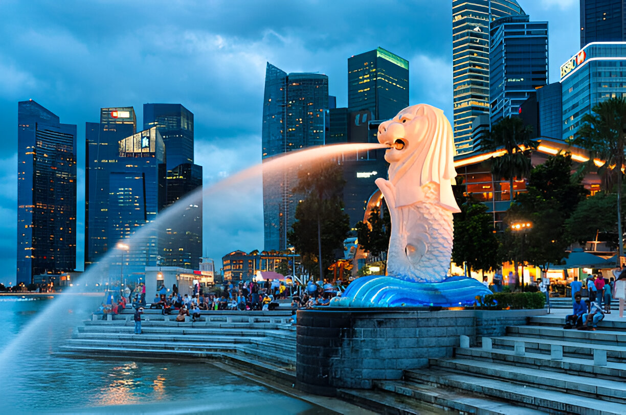 The Merlion statue spouting water at Marina Bay with modern skyscrapers in the background during twilight