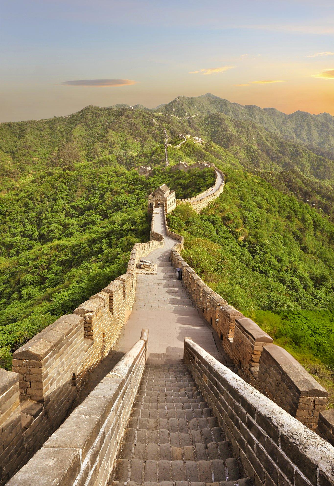 Scenic view of the Great Wall of China winding through lush green mountains under a golden sky