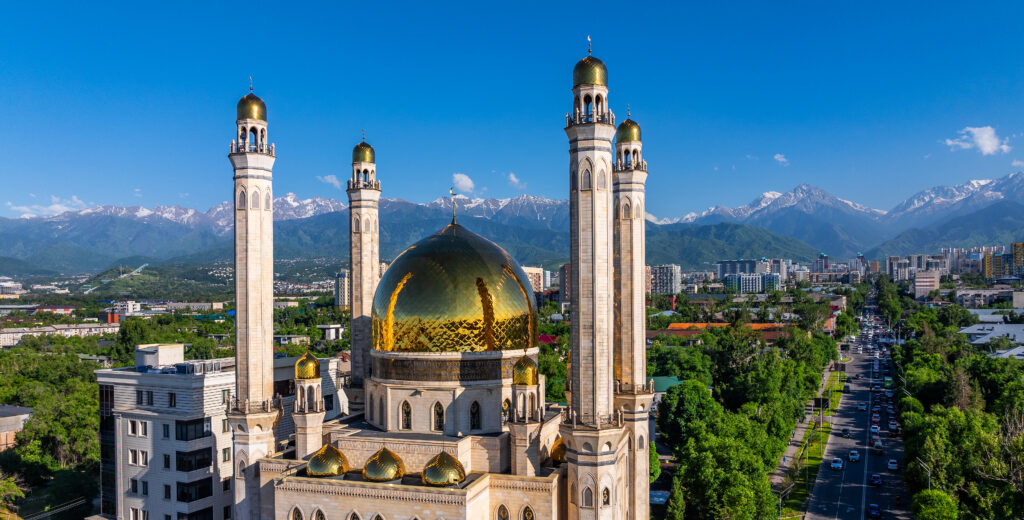 Central Mosque of Almaty with snow-capped mountains in the background under clear blue skies