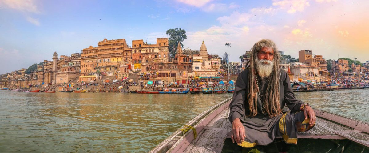 A holy sadhu on a wooden boat with the Varanasi ghats in the background at sunset